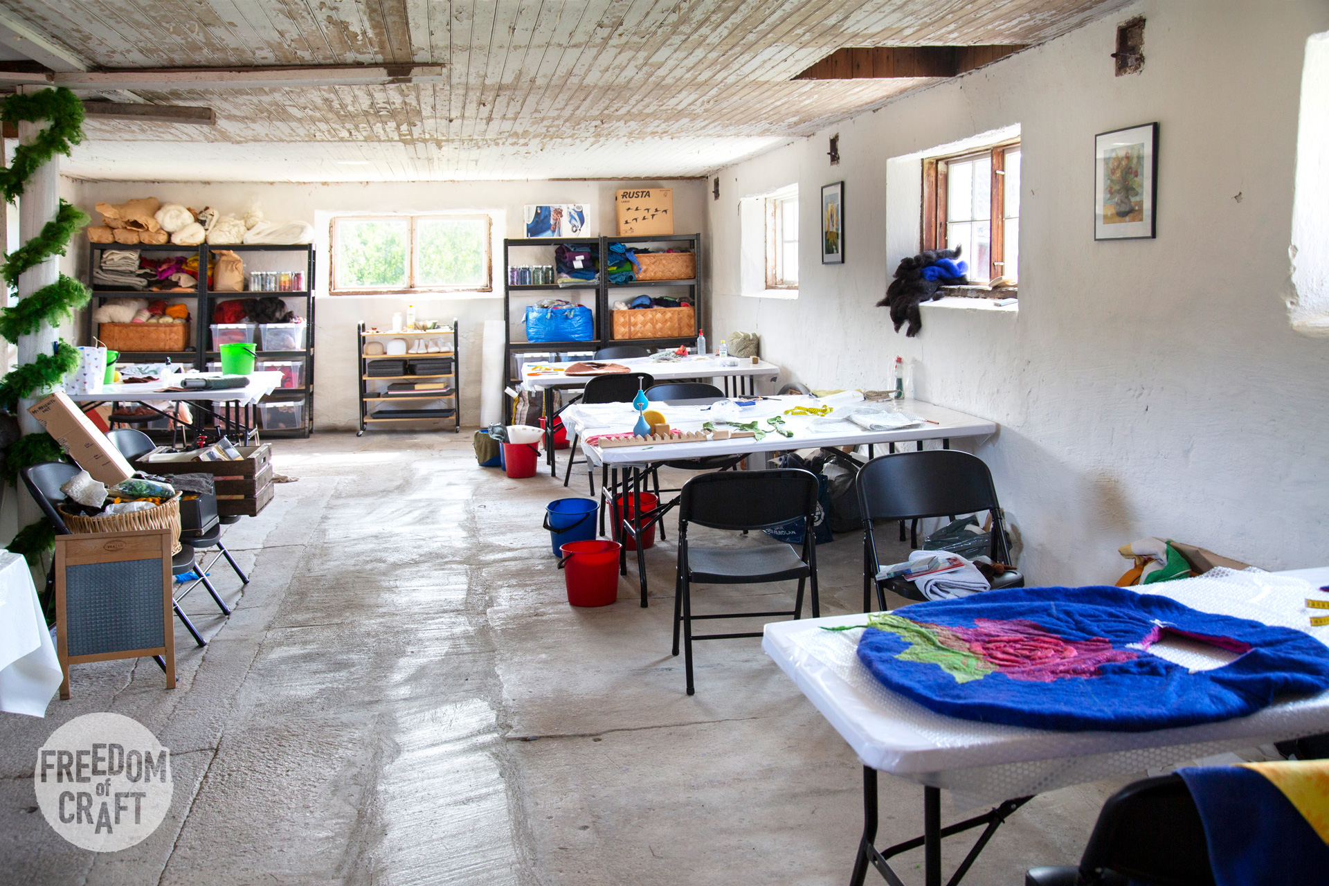 The atelier. A view into a room with concrete floor, white walls and tables placed to the right. Students works is on the tables. In the far back, materials are on display.